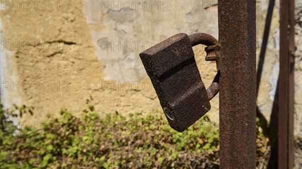 Rusted lock on a metal post in front of a weathered wall with plants in the background, Old silk factory, German Wehrmacht military prison, concentration camp, Lost Place, Kattavia, Rhodes, Dodecanese, Greek Islands, Greece