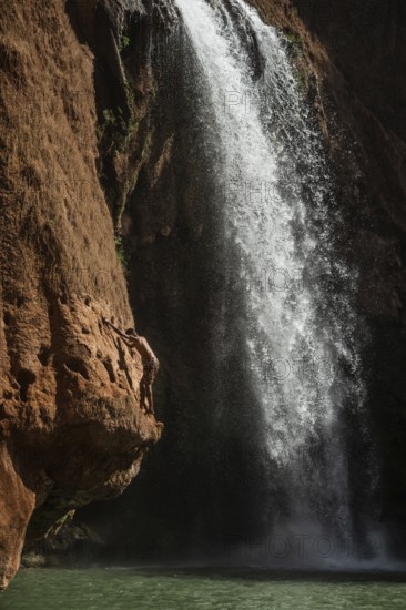 A Moroccan young man climbs the rock before jump from into the water under a waterfall Ouzoud