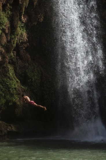 A Moroccan young man jumps from the high rock into the water under a waterfall Ouzoud