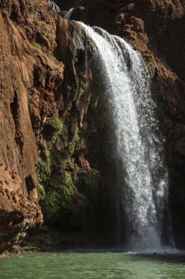 Moroccan young man jumps from the high rock into the water under a waterfall Ouzoud