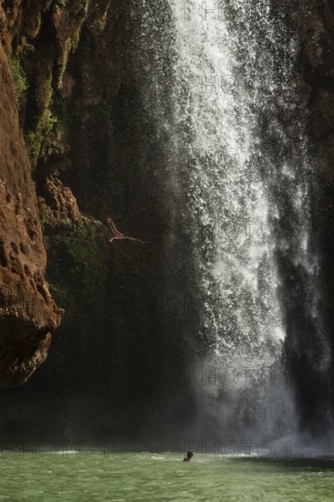 Moroccan young man jumps from the high rock into the water under a waterfall Ouzoud