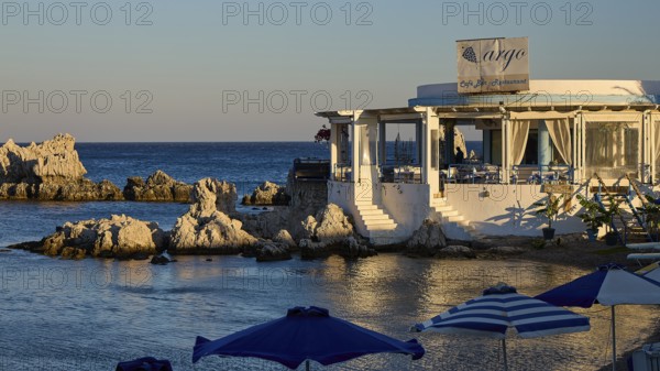 Restaurant Argo, Cosy restaurant by the sea with rocks in the water and evening sun, protected by umbrellas, bay, Charaki, Haraki, east coast Rhodes, Rhodes, Dodecanese, Greek Islands, Greece