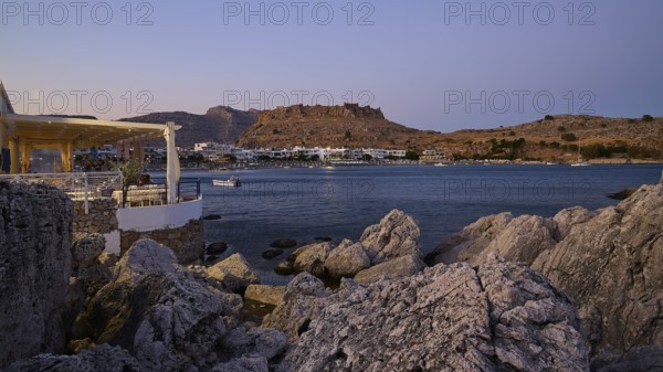 Restaurant Argo, Rock-framed view of a coastal town and sea at dusk, bay, Feraklos fortress, Charaki, Haraki, east coast of Rhodes, Rhodes, Dodecanese, Greek Islands, Greece