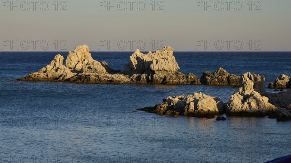 Large rock formations rise out of the calm blue sea under the soft evening light, Charaki Bay, Haraki, East Coast of Rhodes, Rhodes, Dodecanese, Greek Islands, Greece