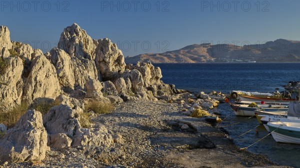 Rocky landscape by the sea with boats and view of distant mountain ranges, bay, Charaki, Haraki, east coast Rhodes, Rhodes, Dodecanese, Greek Islands, Greece