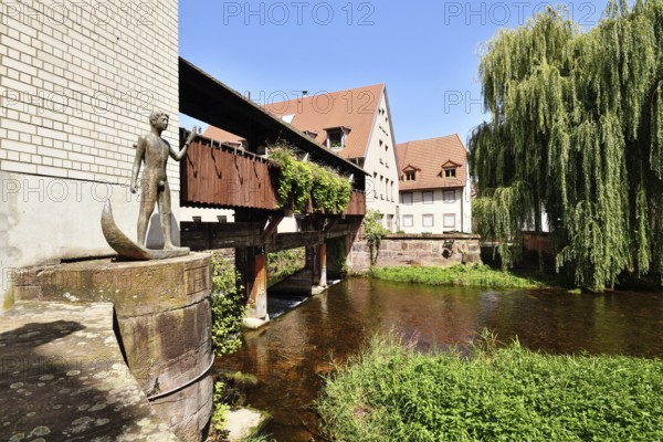 Ettlingen, Germany - August 13th 2025: Historic old town of Ettlingen Germany with wooden bridge over Alb river and sculpture of man holding fish