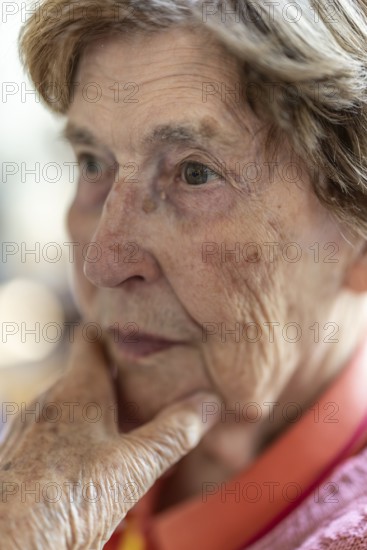 Close-up, authentic, unposed portrait of a 90+ year old senior woman with dementia and Alzheimer's disease in a retirement home, holding a hand to her face, Cologne, North Rhine-Westphalia, Germany