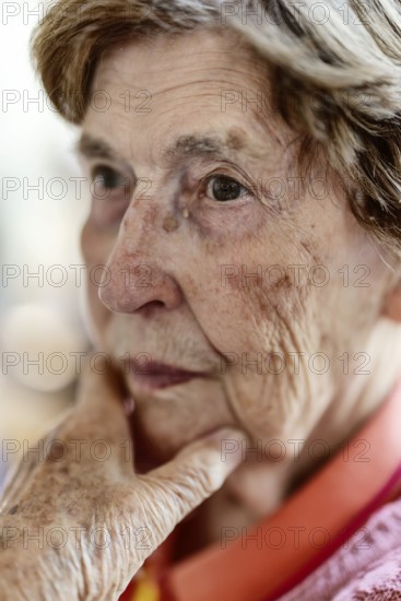 Close-up, authentic, unposed portrait of a 90+ year old senior woman with dementia and Alzheimer's disease in a retirement home, holding a hand to her face, Cologne, North Rhine-Westphalia, Germany