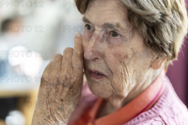 Close-up, authentic, unposed portrait of a 90+ year old senior woman with dementia and Alzheimer's disease in a retirement home, holding a hand to her face, Cologne, North Rhine-Westphalia, Germany