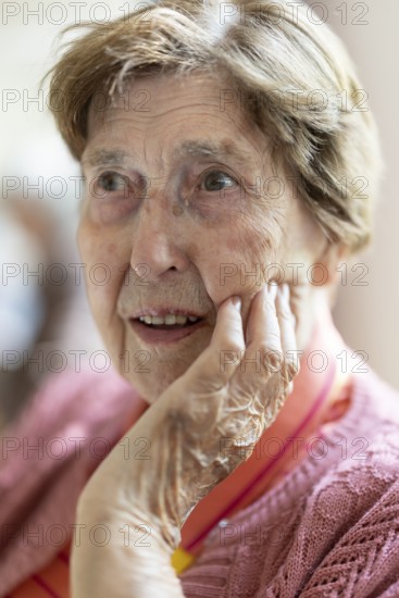 Close-up, authentic, unposed portrait of a 90+ year old senior woman with dementia and Alzheimer's disease in a retirement home, holding a hand to her face, Cologne, North Rhine-Westphalia, Germany