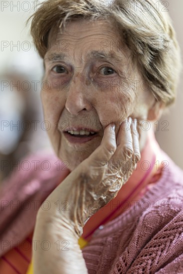 Close-up, authentic, unposed portrait of a 90+ year old senior woman with dementia and Alzheimer's disease in a retirement home, holding a hand to her face, Cologne, North Rhine-Westphalia, Germany