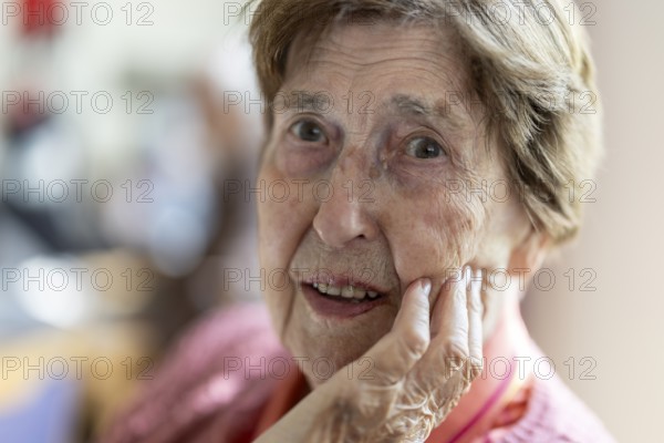 Close-up, authentic, unposed portrait of a 90+ year old senior woman with dementia and Alzheimer's disease in a retirement home, holding a hand to her face, Cologne, North Rhine-Westphalia, Germany
