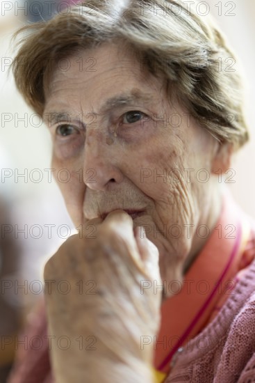 Close-up, authentic, unposed portrait of a 90+ year old senior woman with dementia and Alzheimer's disease in a retirement home, holding a hand to her face, Cologne, North Rhine-Westphalia, Germany