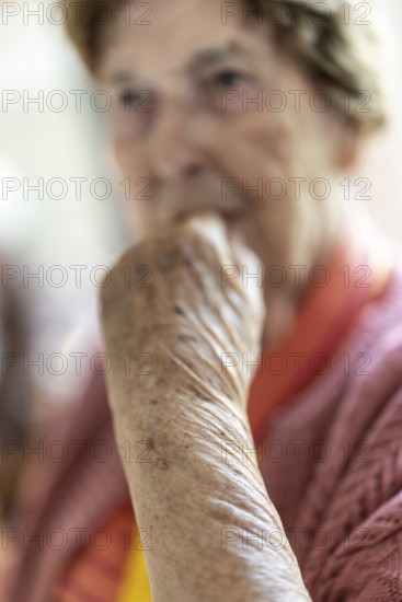 Close-up, authentic, unposed portrait of a 90+ year old senior woman with dementia and Alzheimer's disease in a retirement home, holding a hand to her face, Cologne, North Rhine-Westphalia, Germany
