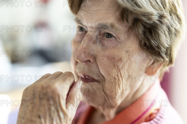 Close-up, authentic, unposed portrait of a 90+ year old senior woman with dementia and Alzheimer's disease in a retirement home, holding a hand to her face, Cologne, North Rhine-Westphalia, Germany