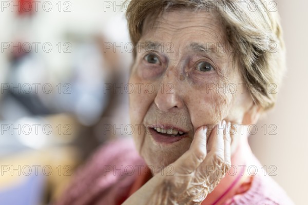 Close-up, authentic, unposed portrait of a 90+ year old senior woman with dementia and Alzheimer's disease in a retirement home, holding a hand to her face, Cologne, North Rhine-Westphalia, Germany