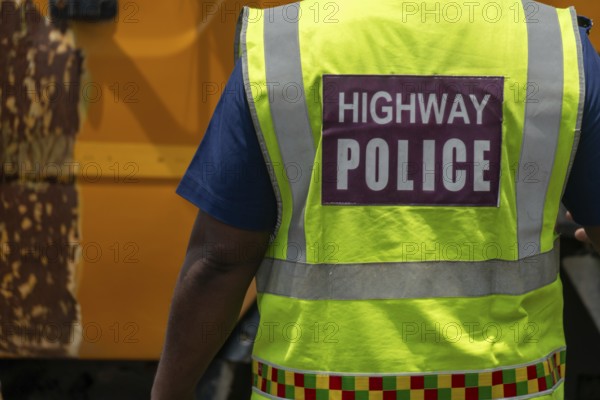 Highway police officer in neon vest with colorful band stands near a vehicle, Dhaka, Bangladesh