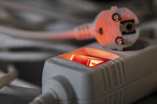 Close-up of a white power plug, Schuko plug, on a multiple socket with red indicator light, symbolic image for electricity, electrical energy, power consumption, studio shot, Germany