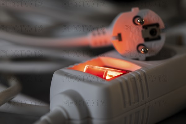 Close-up of a white power plug, Schuko plug, on a multiple socket with red indicator light, symbolic image for electricity, electrical energy, power consumption, studio shot, Germany