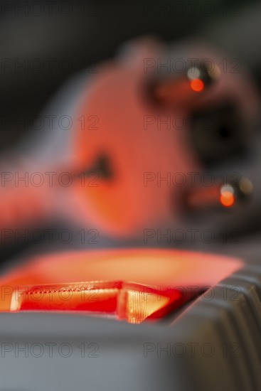 Close-up of a white power plug, Schuko plug, on a multiple socket with red indicator light, symbolic image for electricity, electrical energy, power consumption, studio shot, Germany