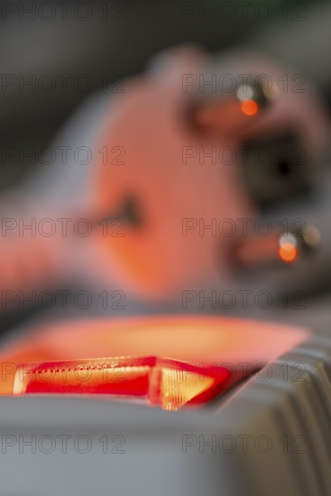 Close-up of a white power plug, Schuko plug, on a multiple socket with red indicator light, symbolic image for electricity, electrical energy, power consumption, studio shot, Germany