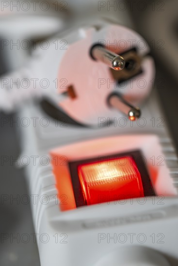 Close-up of a white power plug, Schuko plug, on a multiple socket with red indicator light, symbolic image for electricity, electrical energy, power consumption, studio shot, Germany
