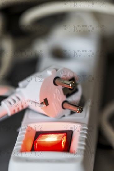 Close-up of a white power plug, Schuko plug, on a multiple socket with red indicator light, symbolic image for electricity, electrical energy, power consumption, studio shot, Germany