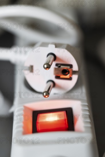 Close-up of a white power plug, Schuko plug, on a multiple socket with red indicator light, symbolic image for electricity, electrical energy, power consumption, studio shot, Germany