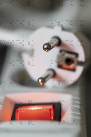 Close-up of a white power plug, Schuko plug, on a multiple socket with red indicator light, symbolic image for electricity, electrical energy, power consumption, studio shot, Germany