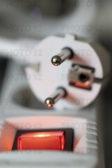 Close-up of a white power plug, Schuko plug, on a multiple socket with red indicator light, symbolic image for electricity, electrical energy, power consumption, studio shot, Germany