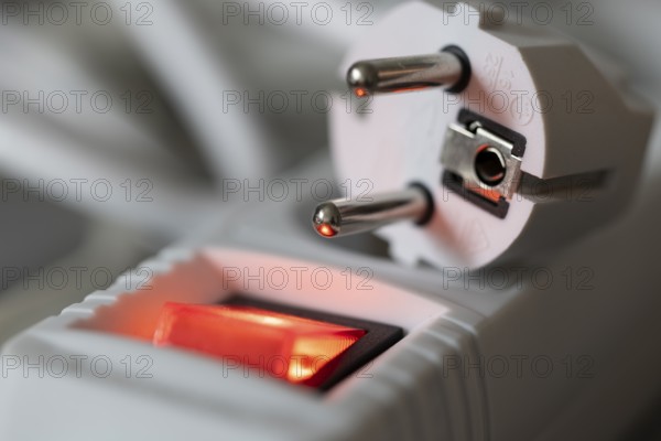 Close-up of a white power plug, Schuko plug, on a multiple socket with red indicator light, symbolic image for electricity, electrical energy, power consumption, studio shot, Germany