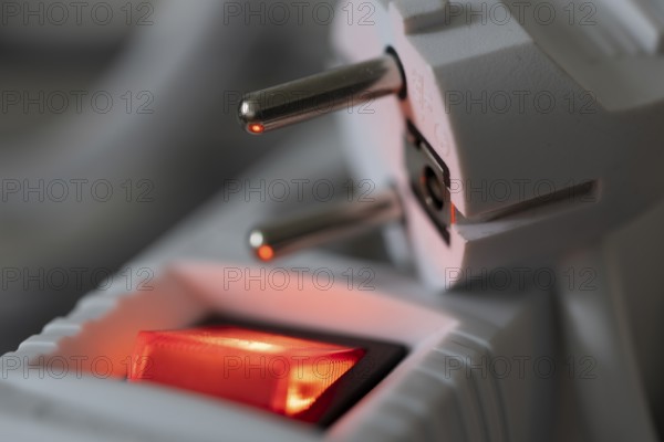 Close-up of a white power plug, Schuko plug, on a multiple socket with red indicator light, symbolic image for electricity, electrical energy, power consumption, studio shot, Germany