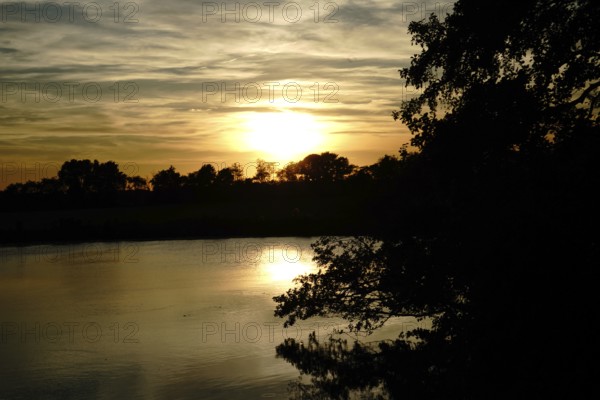 A peaceful sunset over a lake, trees against the evening sky, natural landscape in Wüsting, 27798 Hude, Lower Saxony, Germany