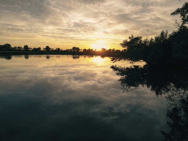 The sun sets over a calm lake and casts gentle reflections on the water, natural landscape in Wüsting, 27798 Hude, Lower Saxony, Germany