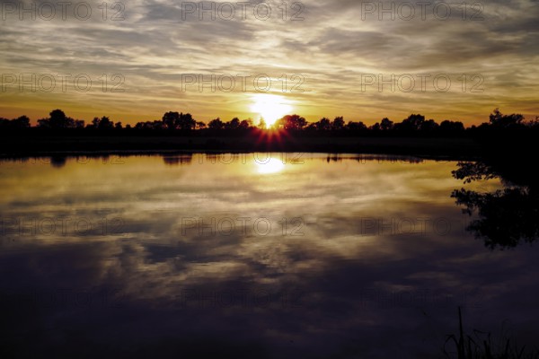 The sunset lights up the sky while the lake reflects the colours, natural landscape in Wüsting, 27798 Hude, Lower Saxony, Germany