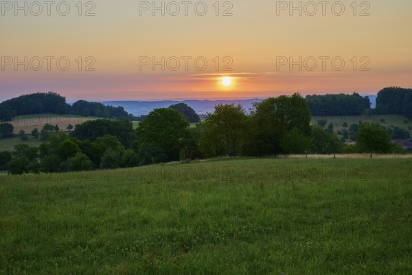 Sun rises over green meadow and wooded valley, colourful sky, Laudenau, Reichelsheim, Odenwald, Hesse, Germany
