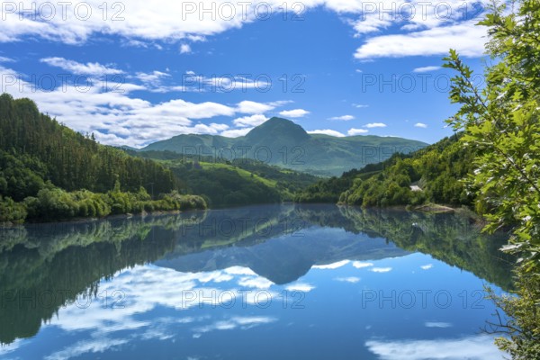 The calm waters of ibiur reservoir perfectly mirror the vibrant blue sky and lush green mountains surrounding it, creating a serene and picturesque scene in tolosa, basque country