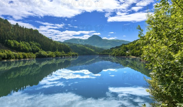 Tranquil ibiur reservoir mirrors the picturesque landscape of lush green hills and vibrant blue sky dotted with fluffy white clouds, creating a breathtaking scene in tolosa, basque country
