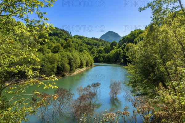 Ibiur reservoir in tolosa, gipuzkoa, basque country, showcases calm waters reflecting lush green hills and a vibrant blue sky on a sunny day, creating a picturesque landscape