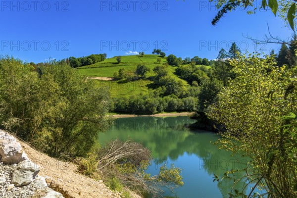 Ibiur reservoir reflects the surrounding green hills and lush vegetation under a clear blue sky, creating a serene and picturesque landscape in tolosa, gipuzkoa, basque country