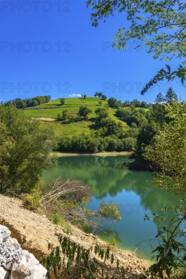 The tranquil waters of ibiur reservoir mirror the vibrant green hills and clear blue sky of the basque country, creating a serene landscape near tolosa, gipuzkoa
