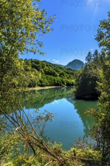 The calm waters of ibiur reservoir reflect the surrounding green hills and vibrant blue sky, creating a serene and picturesque scene in the heart of basque country, spain, on a sunny summer day
