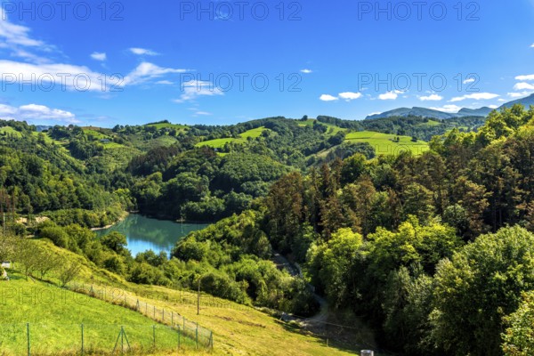 Ibiur reservoir reflects the vibrant blue sky amidst the rolling green hills and lush forests of tolosa, gipuzkoa, in the heart of the basque country, creating a picturesque summer landscape