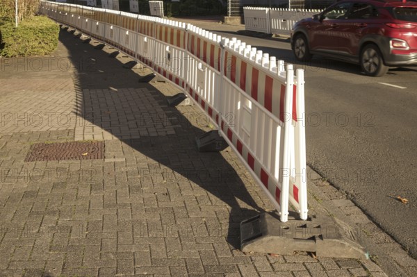 Borken, NRW, Germany, Red and white plastic construction barriers lining a paved walkway beside a road with a passing car, ensuring safety in a work zone