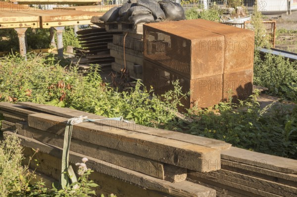 Borken, NRW, Germany, Various construction materials, including wooden planks and rusty metal crates, are stacked on the ground amidst weeds, awaiting use in a construction project
