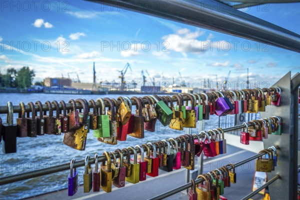 Many colourful love locks on a railing with a view of the harbour and cranes. View from the jetties in St. Pauli, 20359 Hamburg, Germany