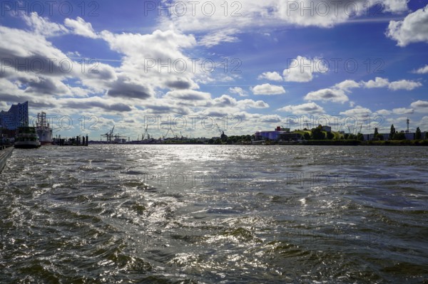 The Norderelbe with wavy water under a sunny sky, with urban background and silhouettes of cranes. View from the Landungsbrücken in St. Pauli, 20359 Hamburg, Germany