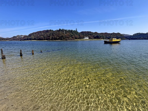 Yellow boat and old wooden piles in a loch with wooded island in the background under blue sky, Silver Sands of Morar, Morar, film set, Scotland, Great Britain
