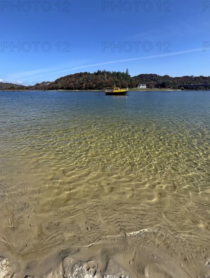 Clear water on a beach with a view of a yellow boat and wooded island in the background, Silver Sands of Morar, Morar, film set, Scotland, United Kingdom