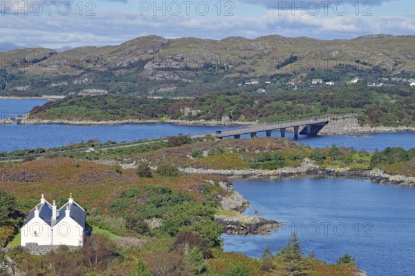 A white house set in a picturesque landscape of bridge, loch and rolling hills under a blue sky, Kyle of Lochalsh, Isle of Skye, Scotland, United Kingdom